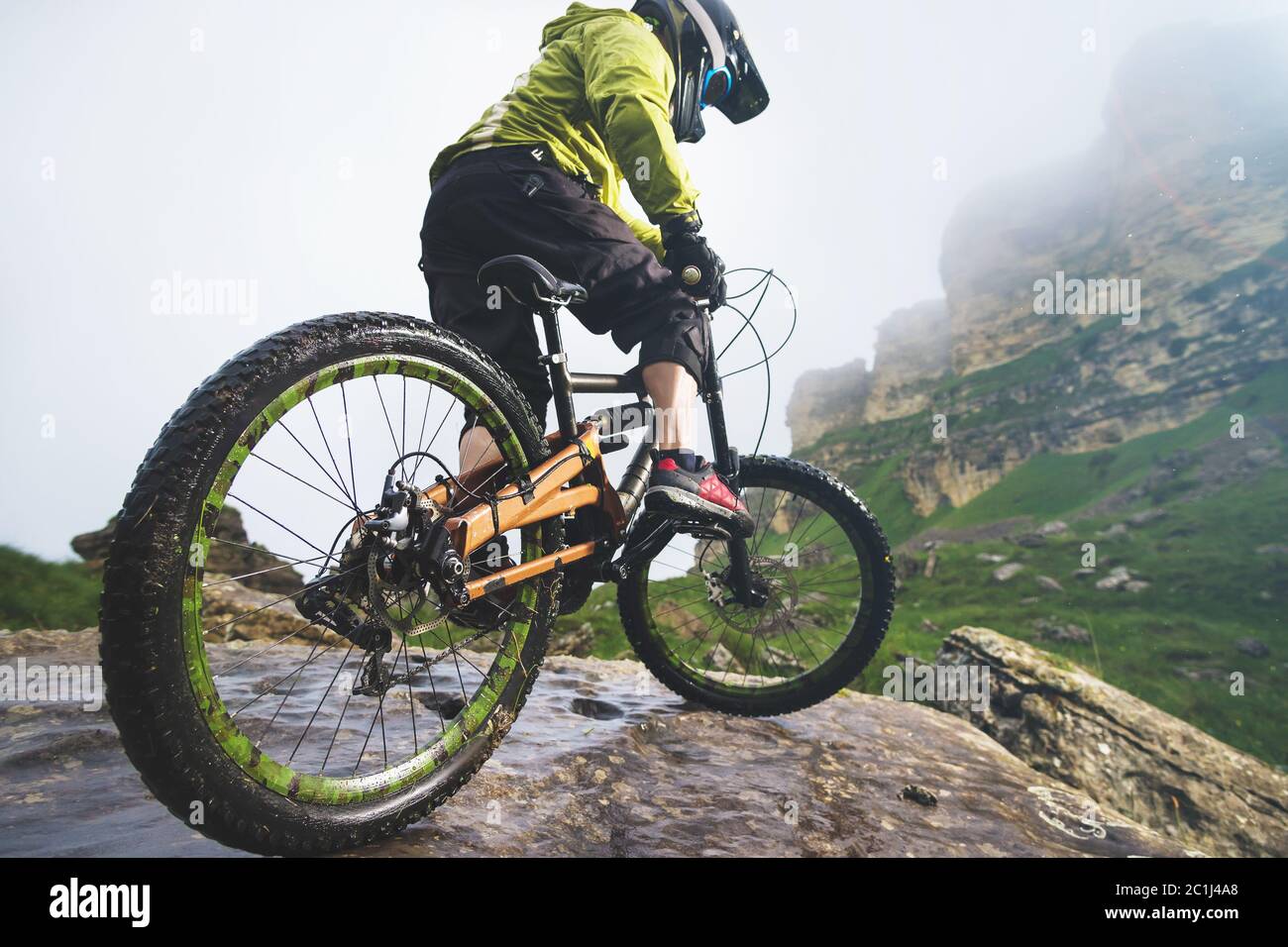 Gambe di ciclisti e ruote posteriori vista ravvicinata della moto mtb posteriore in montagna sullo sfondo di rocce in condizioni atmosferiche nebbie. Il c Foto Stock