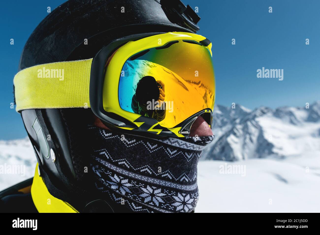 Ritratto di uno sciatore in maschera e casco con faccia chiusa su uno sfondo di montagne innevate e cielo blu Foto Stock
