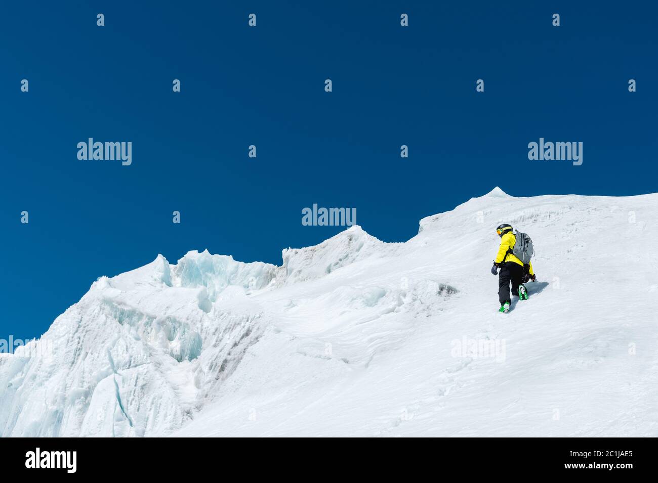 Uno sciatore in un casco e maschera con uno zaino si erge su un pendio sullo sfondo della neve e di un ghiacciaio. Freeride backcountry Foto Stock