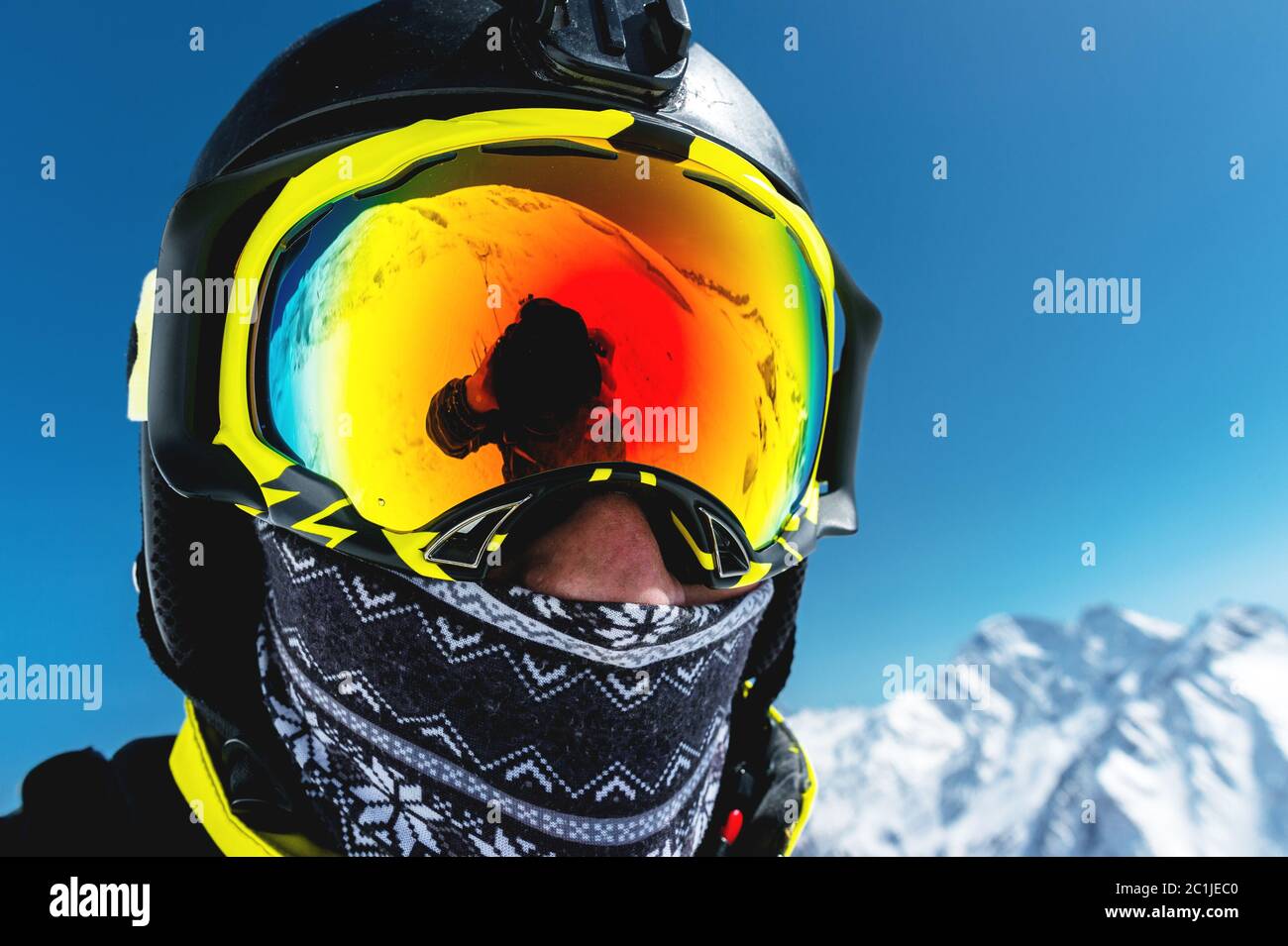 Ritratto di uno sciatore in maschera e casco con faccia chiusa su uno sfondo di montagne innevate e cielo blu Foto Stock