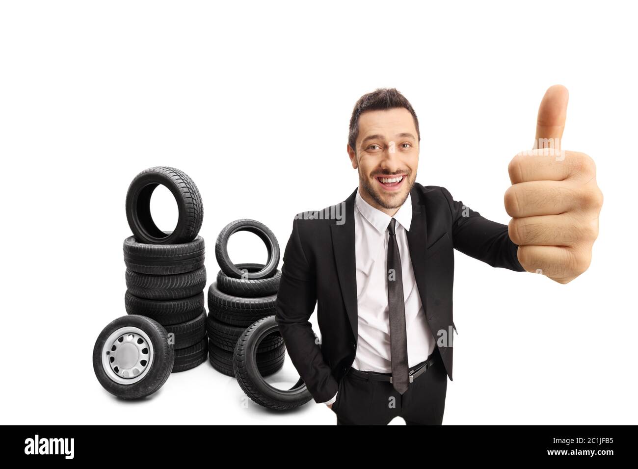 Uomo d'affari che fa un pollice in su segno e posa con le gomme dell'automobile isolate su sfondo bianco Foto Stock