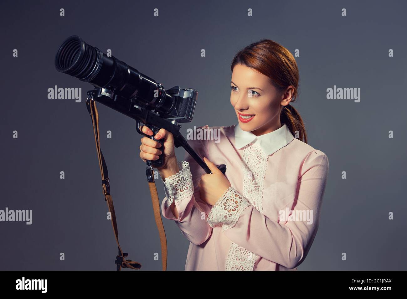 Profilo laterale di una giovane donna che guarda in una fotocamera professionale per scattare foto. Modello misto isolato su sfondo grigio con spazio di copia. Horizont Foto Stock