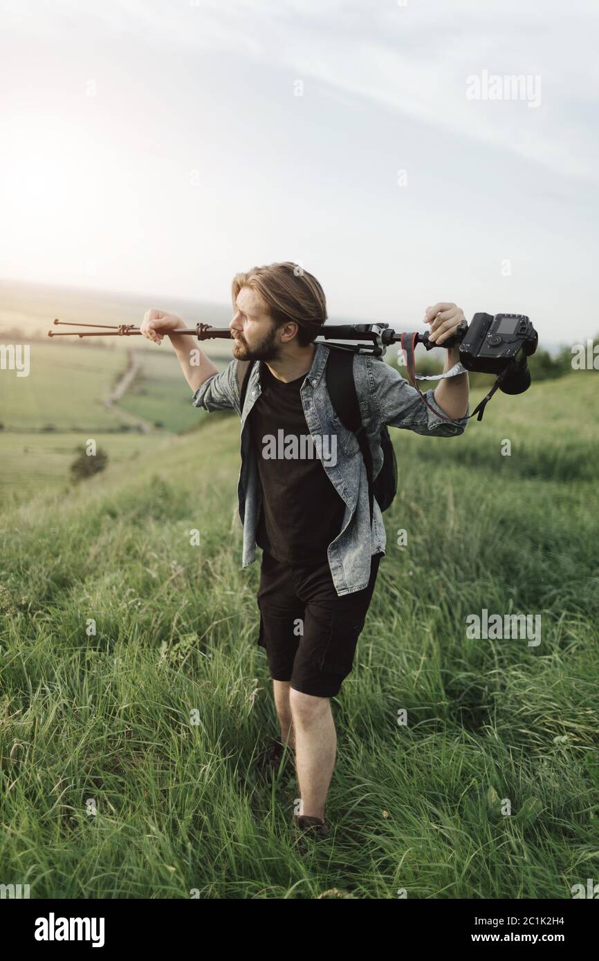 Uomo stanco che tiene il treppiede con la macchina fotografica mentre si arrampica su collina Foto Stock