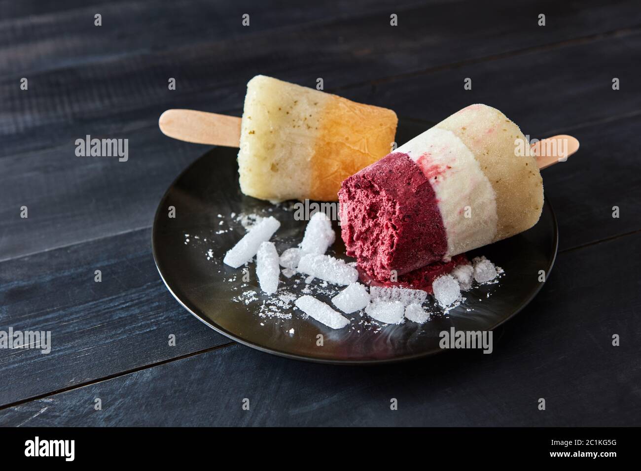 Caffè di frutta gelato fatto in casa su un bastone in un piatto nero con fette di ghiaccio su un tavolo scuro di legno con spazio copia. Col Foto Stock