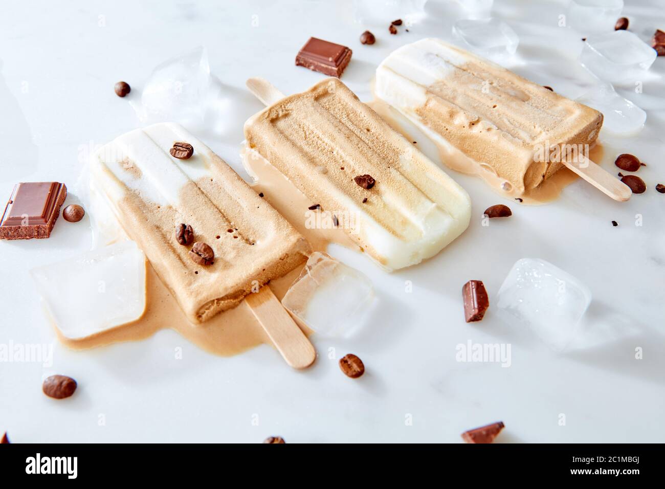 Caffè vegano banana cremoso latte libero ghiaccio schioccato su ghiaccio e marmo sfondo con pezzo di cioccolato e caffè in grani Foto Stock