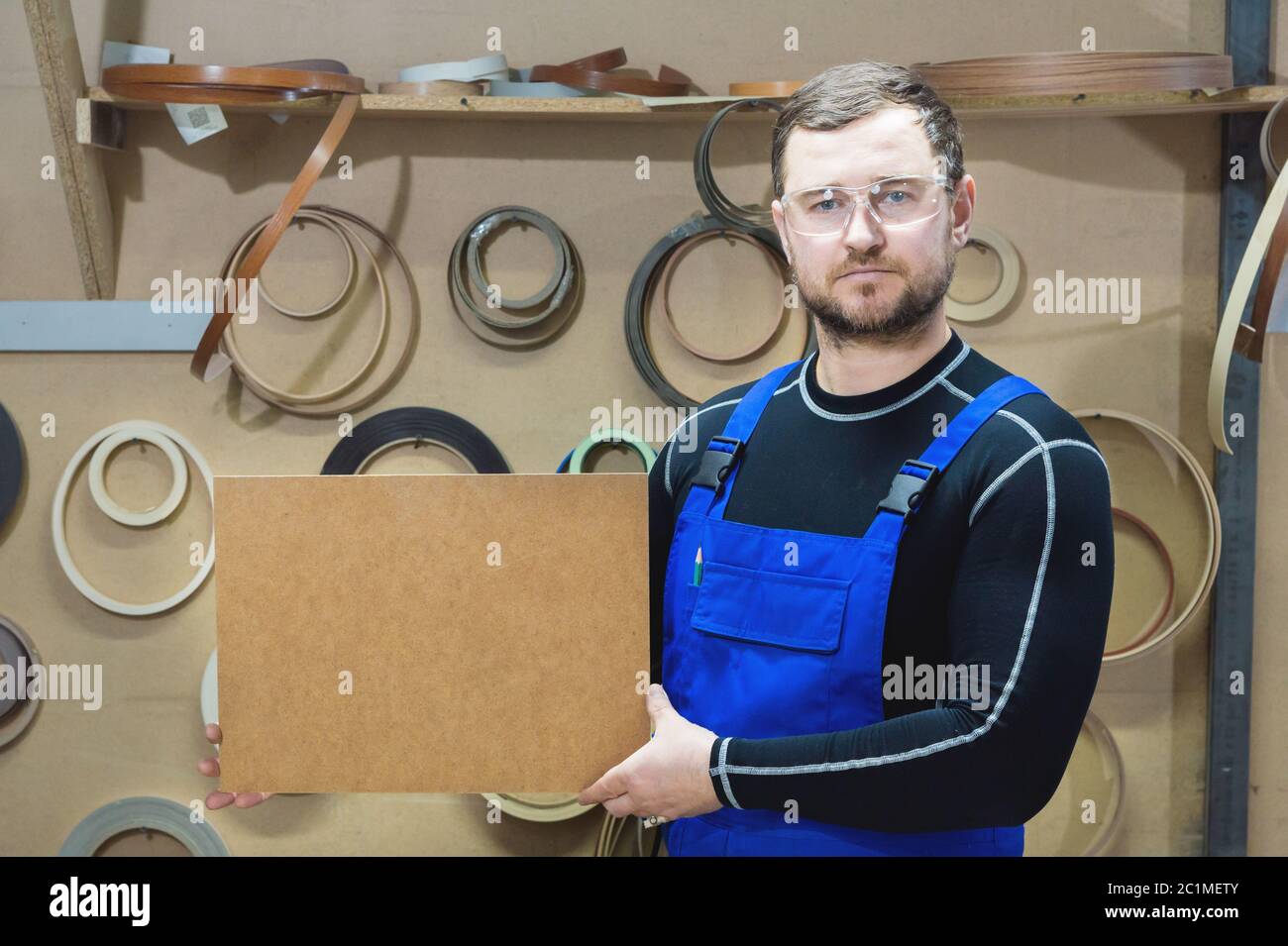 Il produttore di mobili in abiti speciali e occhiali mantiene una piastra vuota per il testo mentre si trova sul posto di lavoro. Imbarcazione p Foto Stock