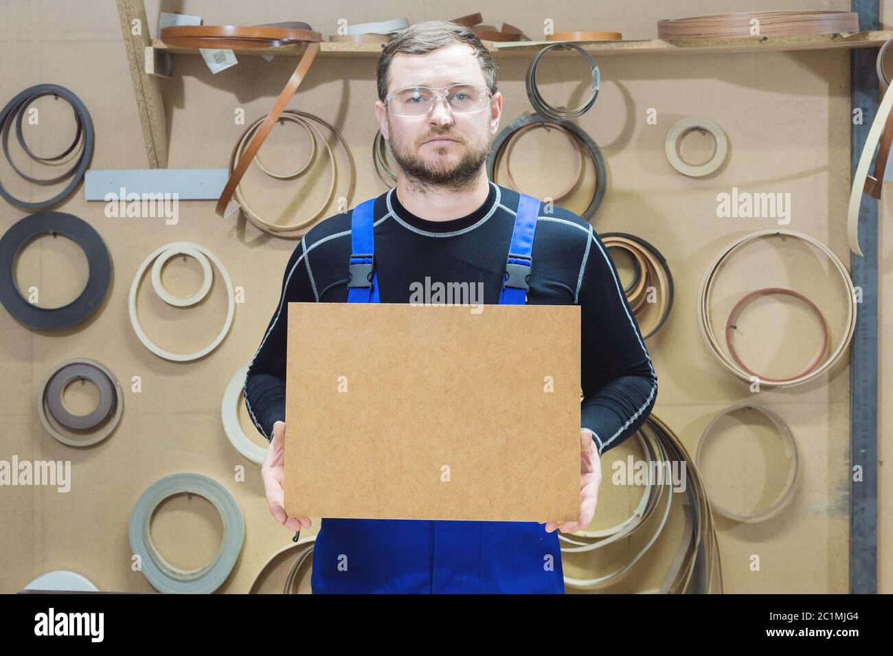 Il produttore di mobili in abiti speciali e occhiali mantiene una piastra vuota per il testo mentre si trova sul posto di lavoro. Imbarcazione p Foto Stock