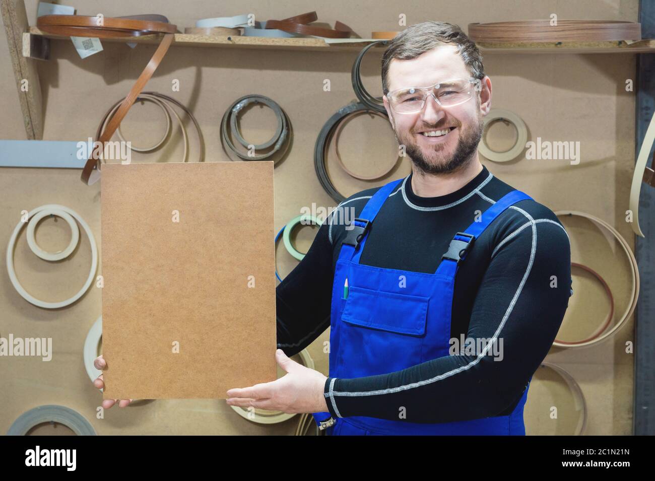 Il produttore di mobili in abiti speciali e occhiali mantiene una piastra vuota per il testo mentre si trova sul posto di lavoro. Imbarcazione p Foto Stock