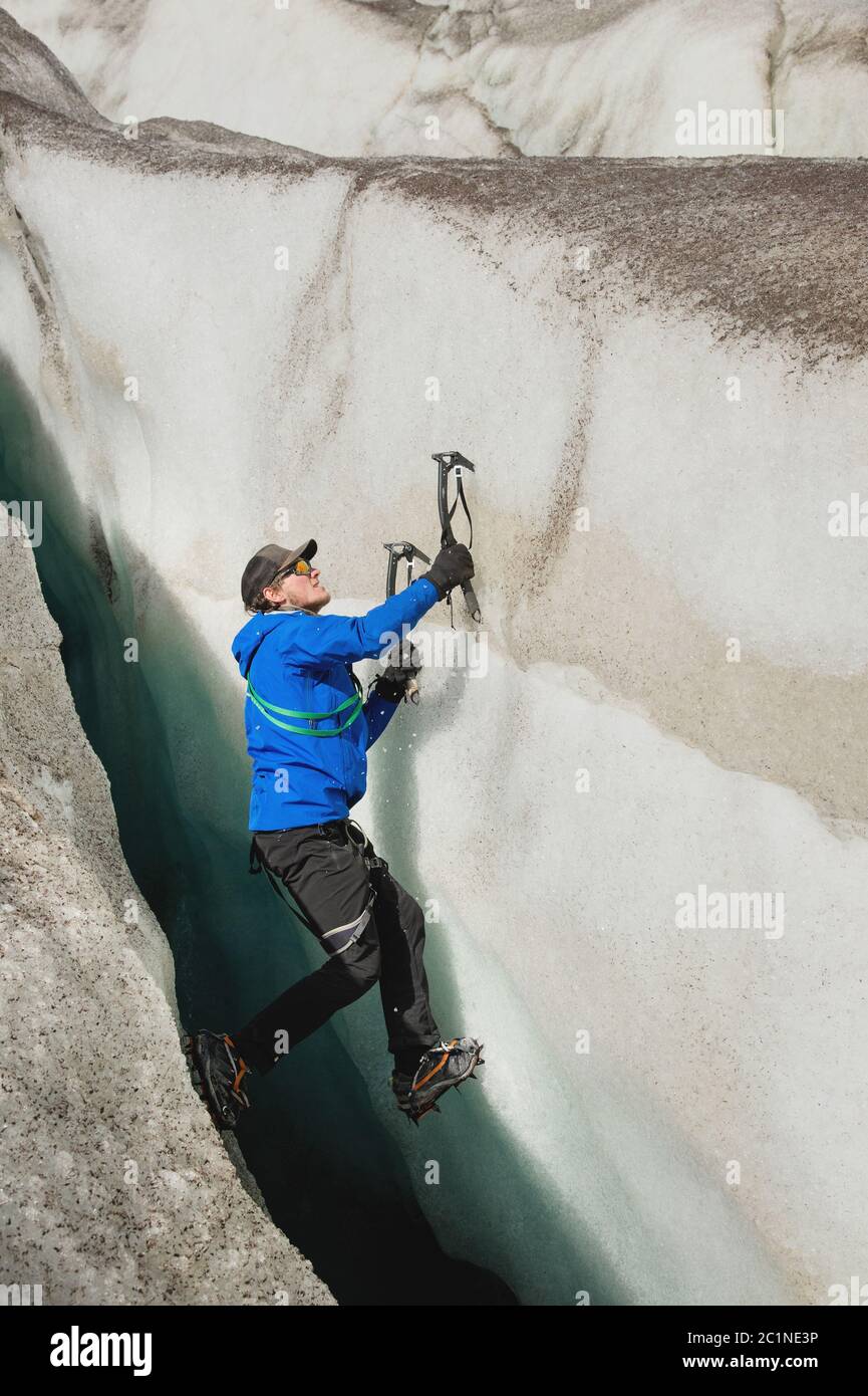 Un arrampicatore libero senza assicurazione con due assi di ghiaccio sale da una crepa nel ghiacciaio. Arrampicata libera senza corde Foto Stock