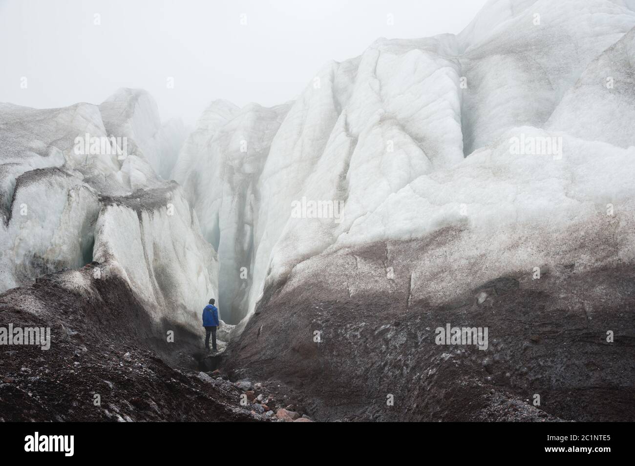 Un arrampicatore libero con un'ascia ghiacciata in mano si trova ai piedi del Grande Ghiacciaio accanto a un'epica crepa nella nebbia nella montagna Foto Stock