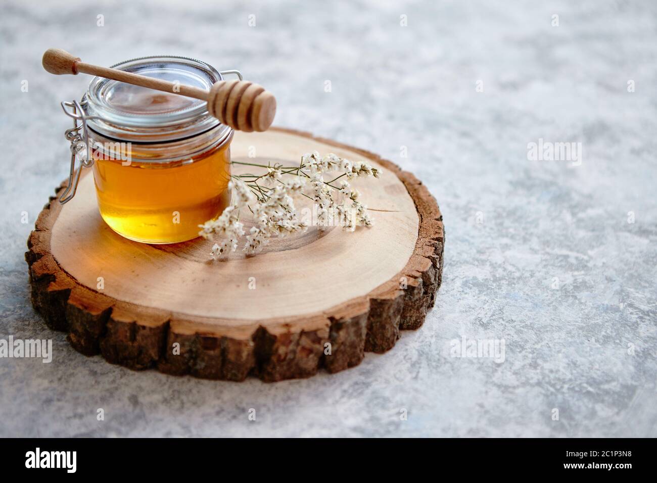 Il vasetto di vetro pieno di miele fresco posto sulla fetta di legno Foto Stock