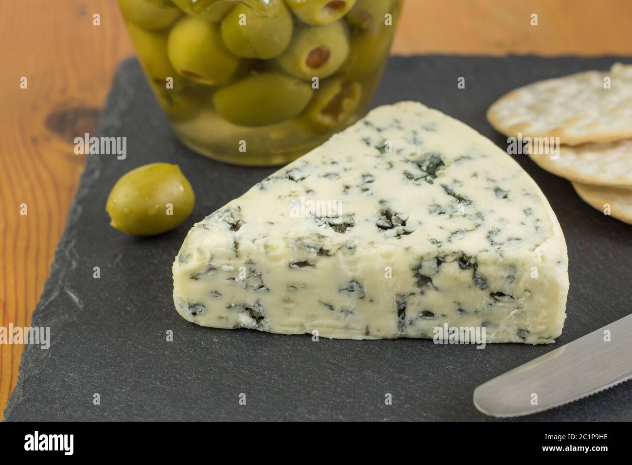 Formaggio blu cuneo con defocalizzata vaso di olive verdi e crackers in background Foto Stock