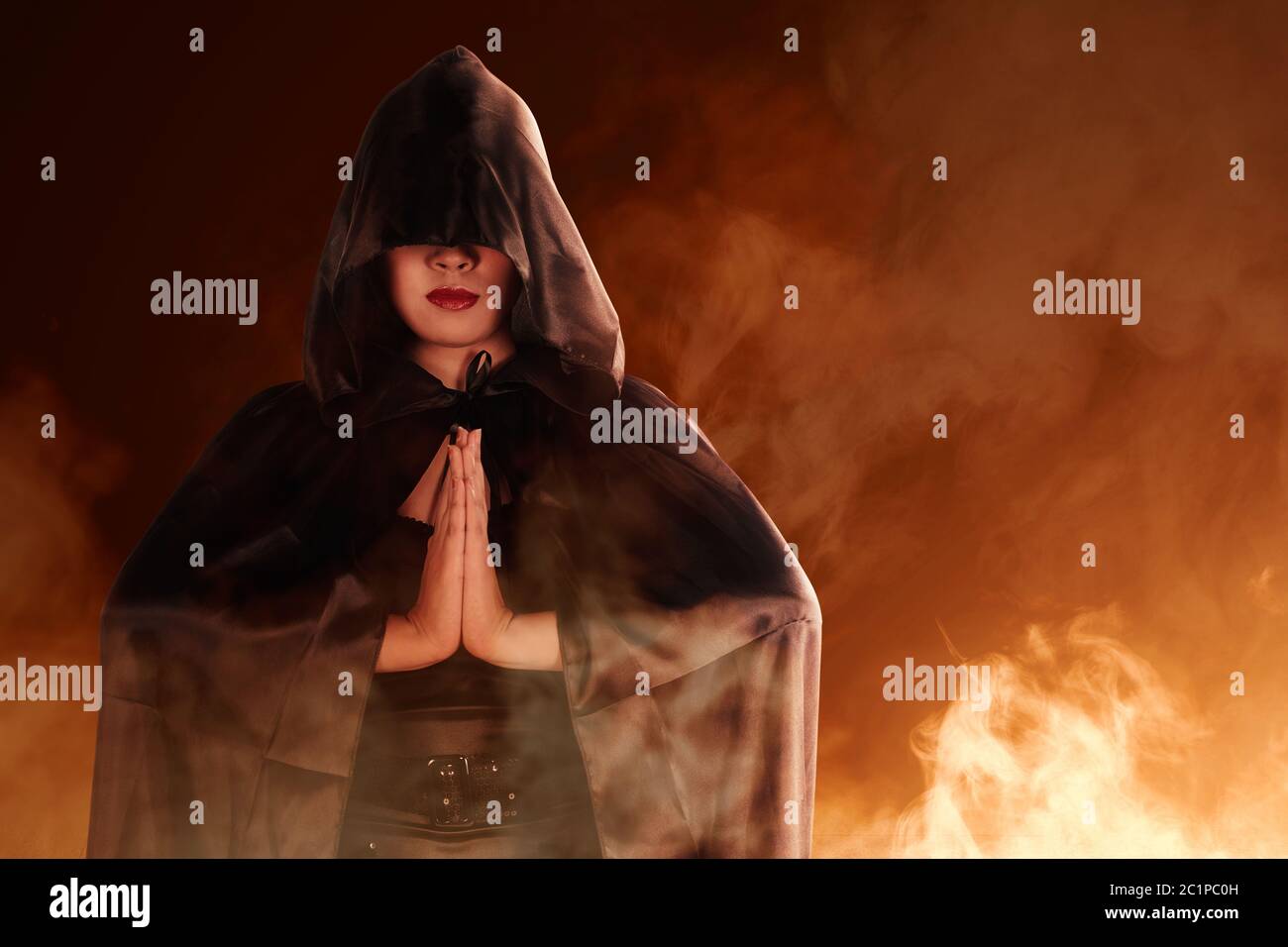 Donna strega asiatica con mantello nero che fa rituale mistico con sfondo di fumo Foto Stock