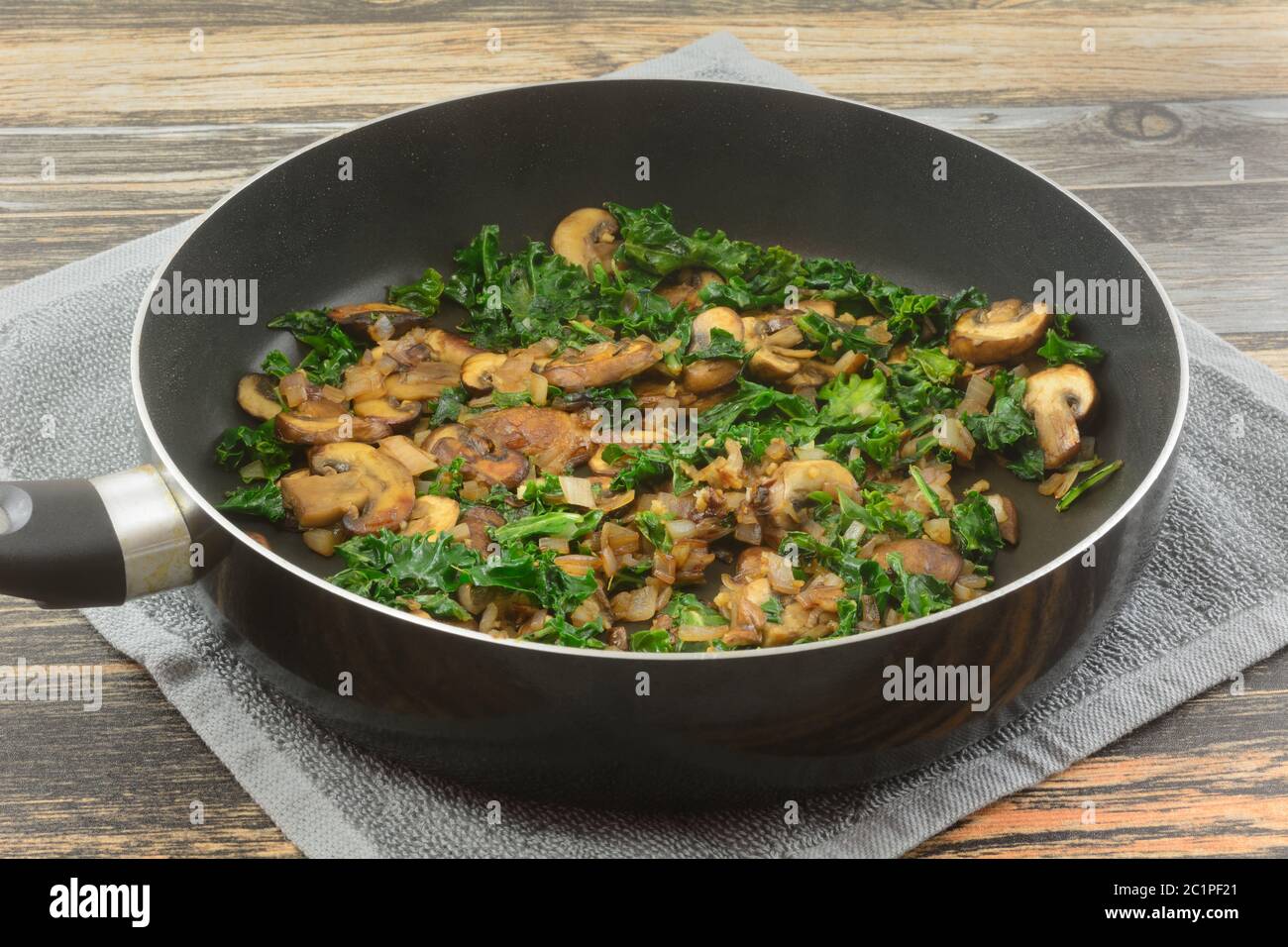 Funghi, ripieno di kale e scalogno o ingrediente saltato in olio d'oliva in padella antiaderente su asciugamano caldo sul tavolo Foto Stock