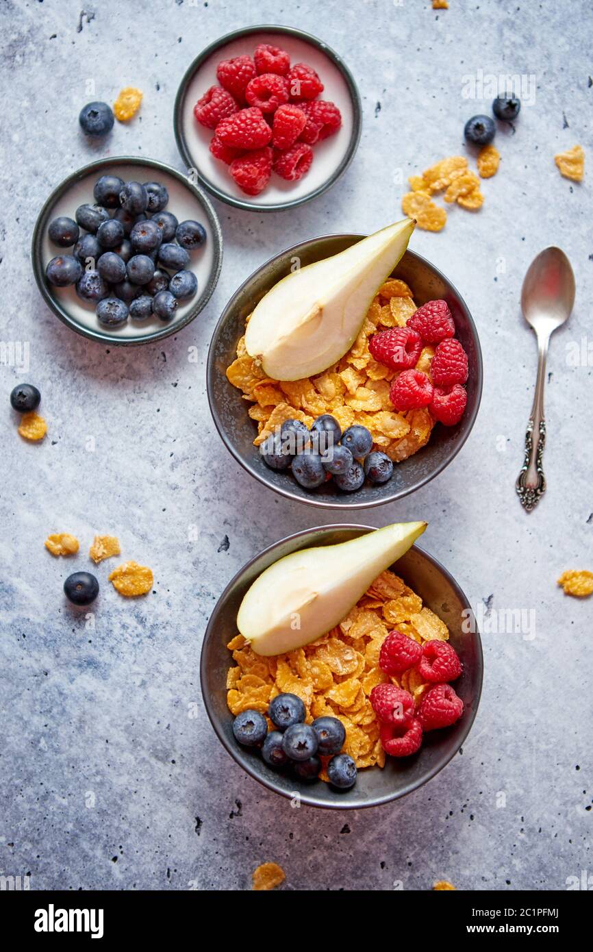 Golden corn flakes con frutti freschi di lamponi mirtilli e pera in vaso in ceramica Foto Stock