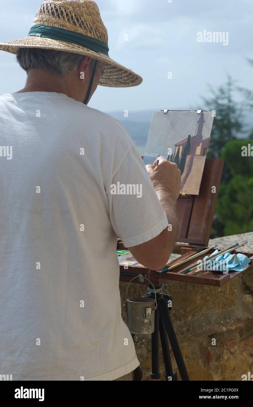 Artista maschile con cappello di paglia dipinge una casa in una strada a  Lucca in Italia in una giornata di sole. Il pannello è su un cavalletto  Foto stock - Alamy