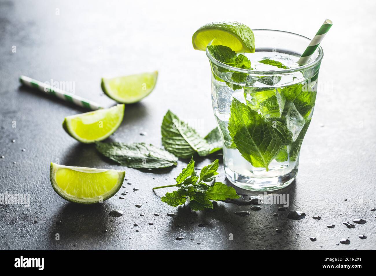 Cocktail con cubetti di lime, menta e ghiaccio su tavolo nero. Foto Stock