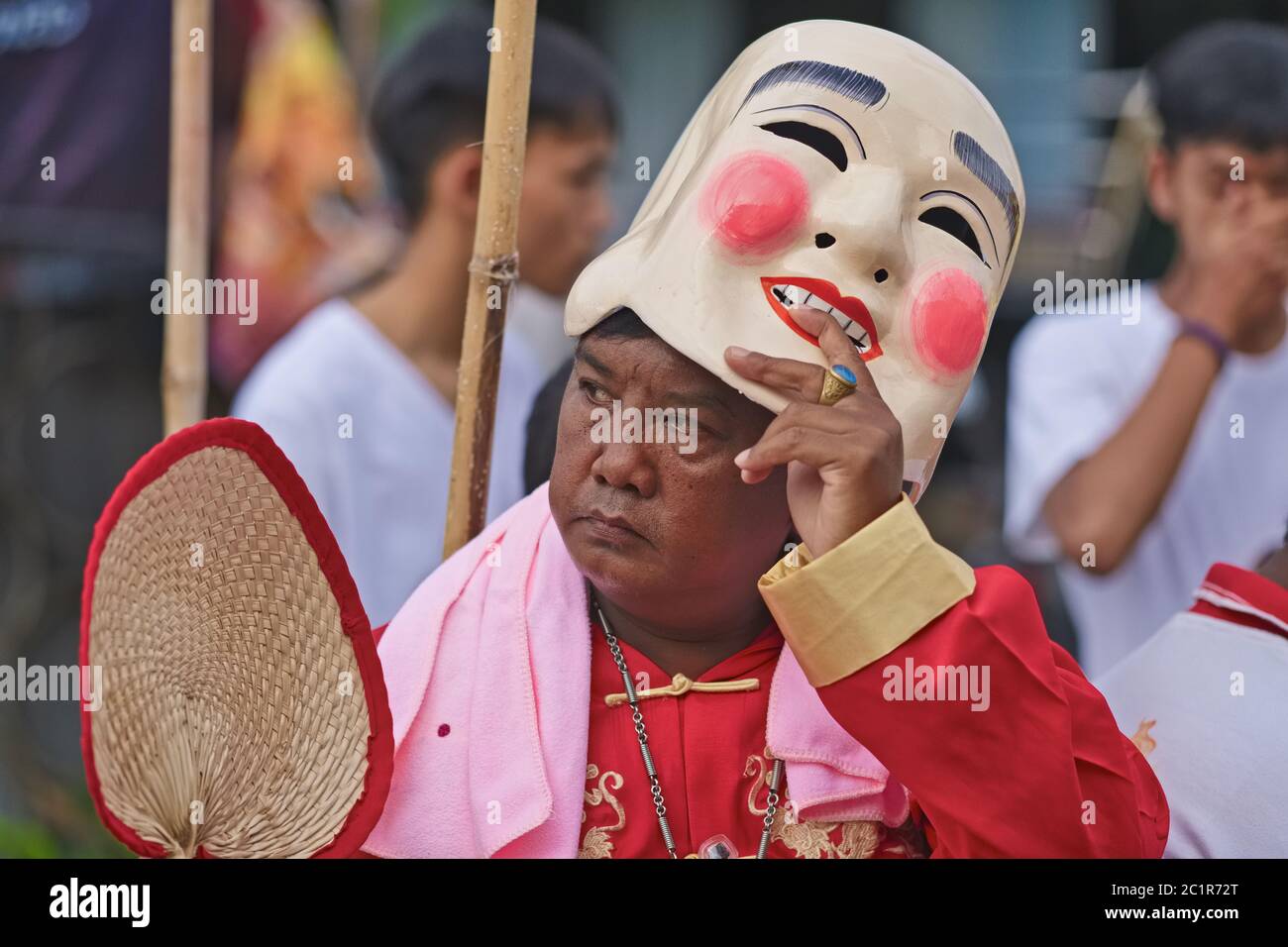 Una processione durante il Festival vegetariano di Phuket, in Thailandia, con un uomo che solleva la sua maschera cinese sorridente per rivelare il suo volto cupo sotto Foto Stock