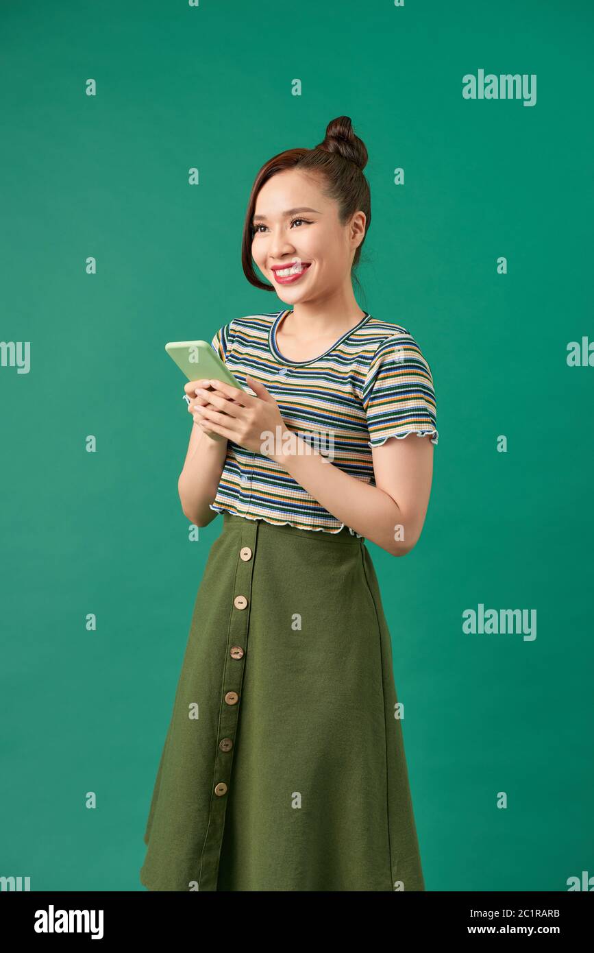 Ritratto di una donna sorridente casual che tiene uno smartphone su sfondo verde Foto Stock