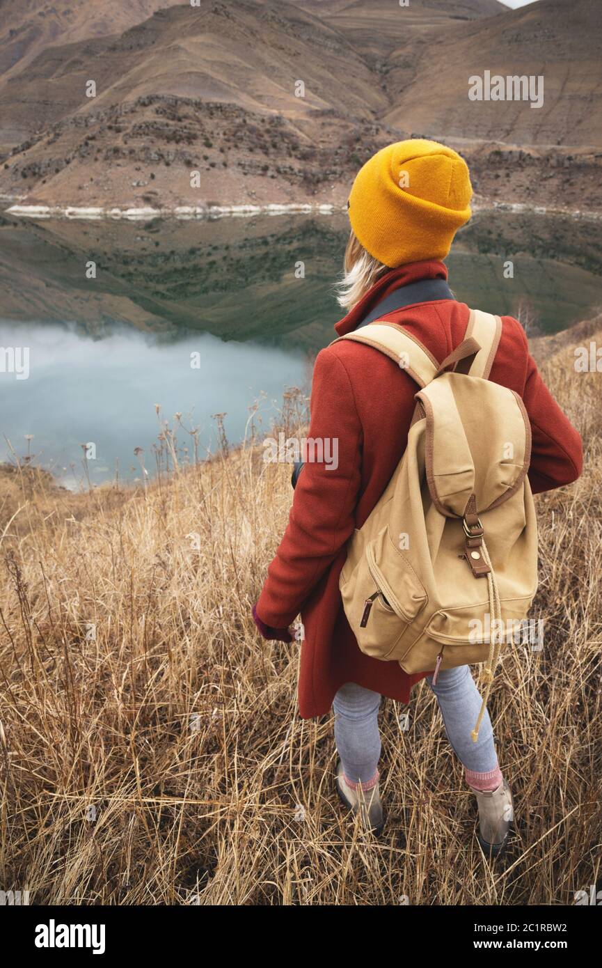 Un ritratto dalla parte posteriore di una ragazza viaggiatore sullo sfondo di un lago in montagna in autunno o all'inizio della primavera. Viaggi conce Foto Stock