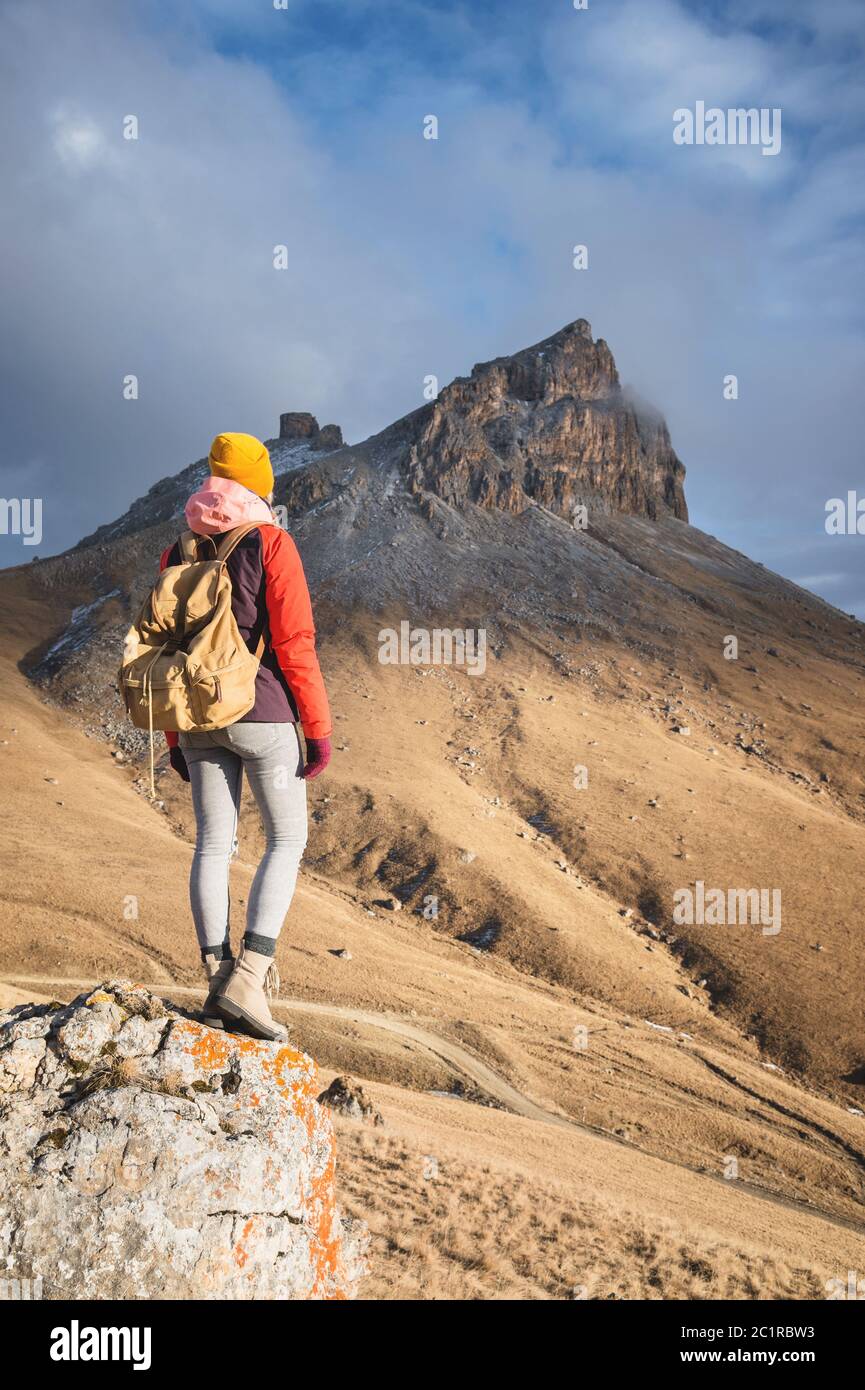 Ritratto dalla parte posteriore di una ragazza viaggiatore in una giacca con un cappello e uno zaino si erge sullo sfondo di un paesaggio epico wi Foto Stock