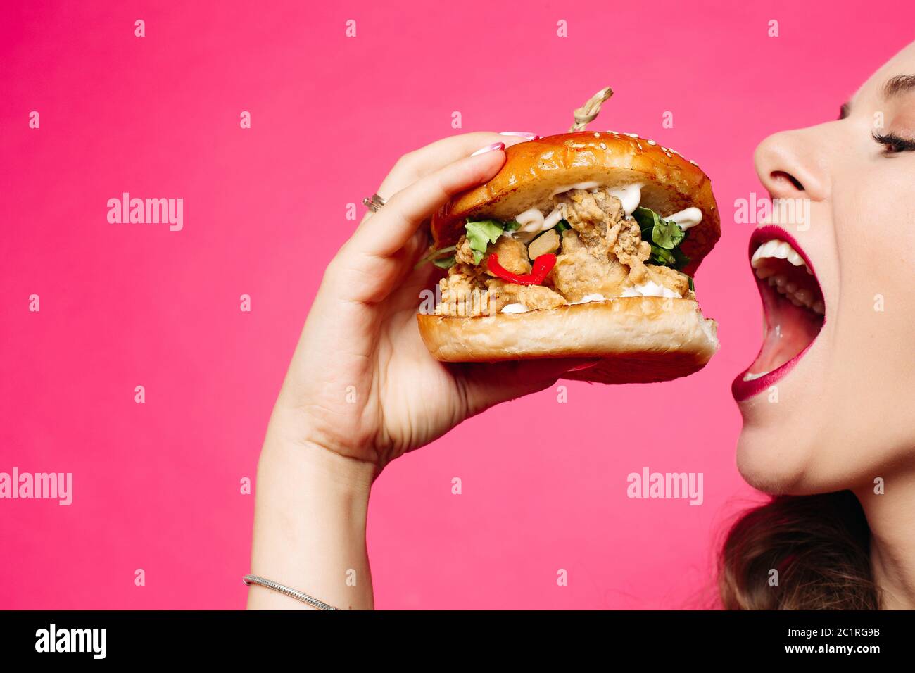 Donna che mangia sandwich. La ragazza felice sta mangiando un hamburger. Aprì la bocca, tenendo un hamburger nella mano destra e loo Foto Stock