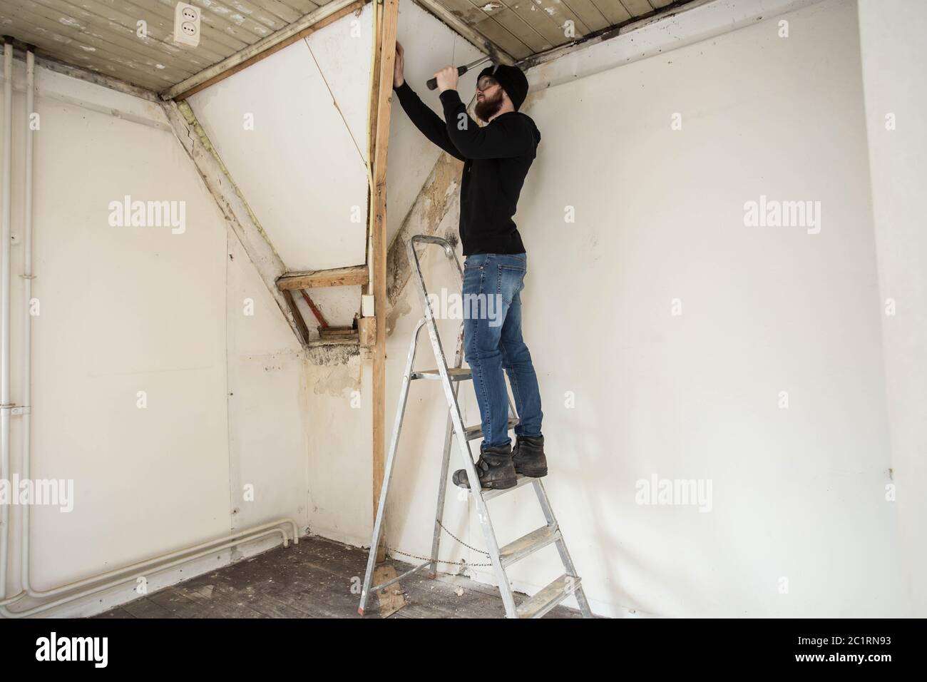 Tuttofare in piedi su una scala e al restauro di una casa, utilizzando strumenti come un martello Foto Stock