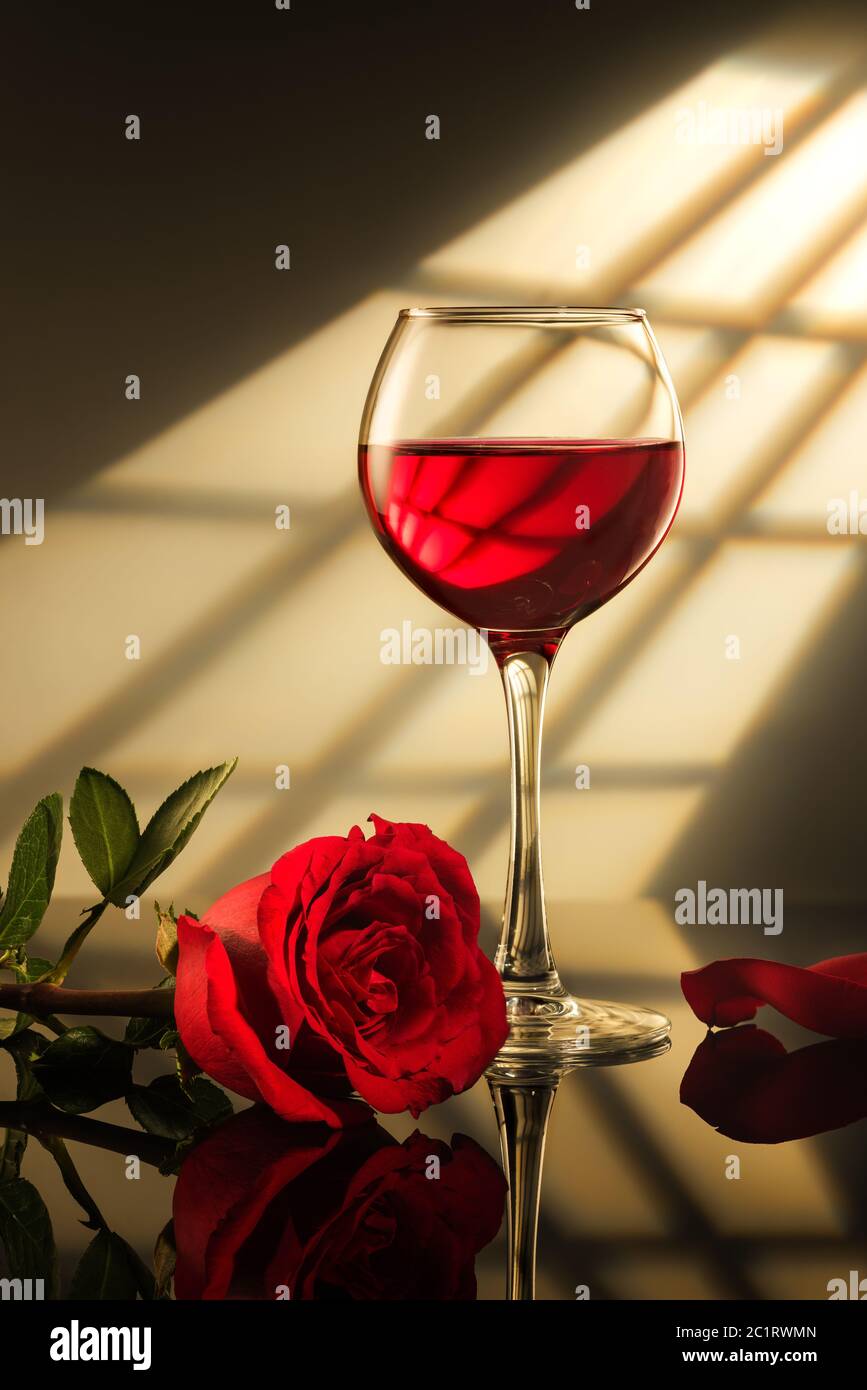 un bicchiere di vino rosso e una rosa rossa sul tavolo con riflessi, luce  dalla finestra Foto stock - Alamy