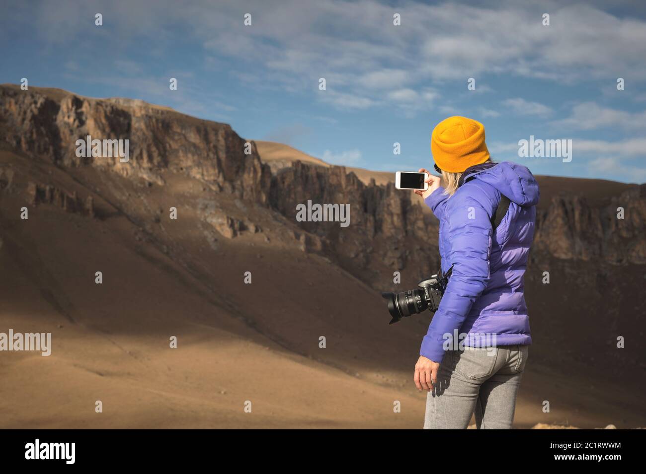 Ritratto dalla parte posteriore di una ragazza in viaggio in una giacca con cappuccio scattando foto di un paesaggio epico con rocce sul suo sm Foto Stock