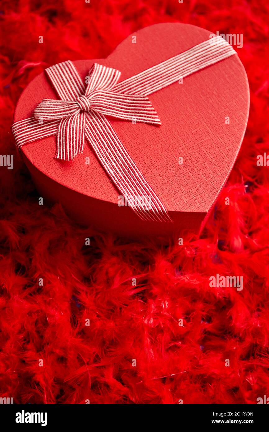 A forma di cuore regalo confezionato, posto sul rosso sfondo piume Foto Stock