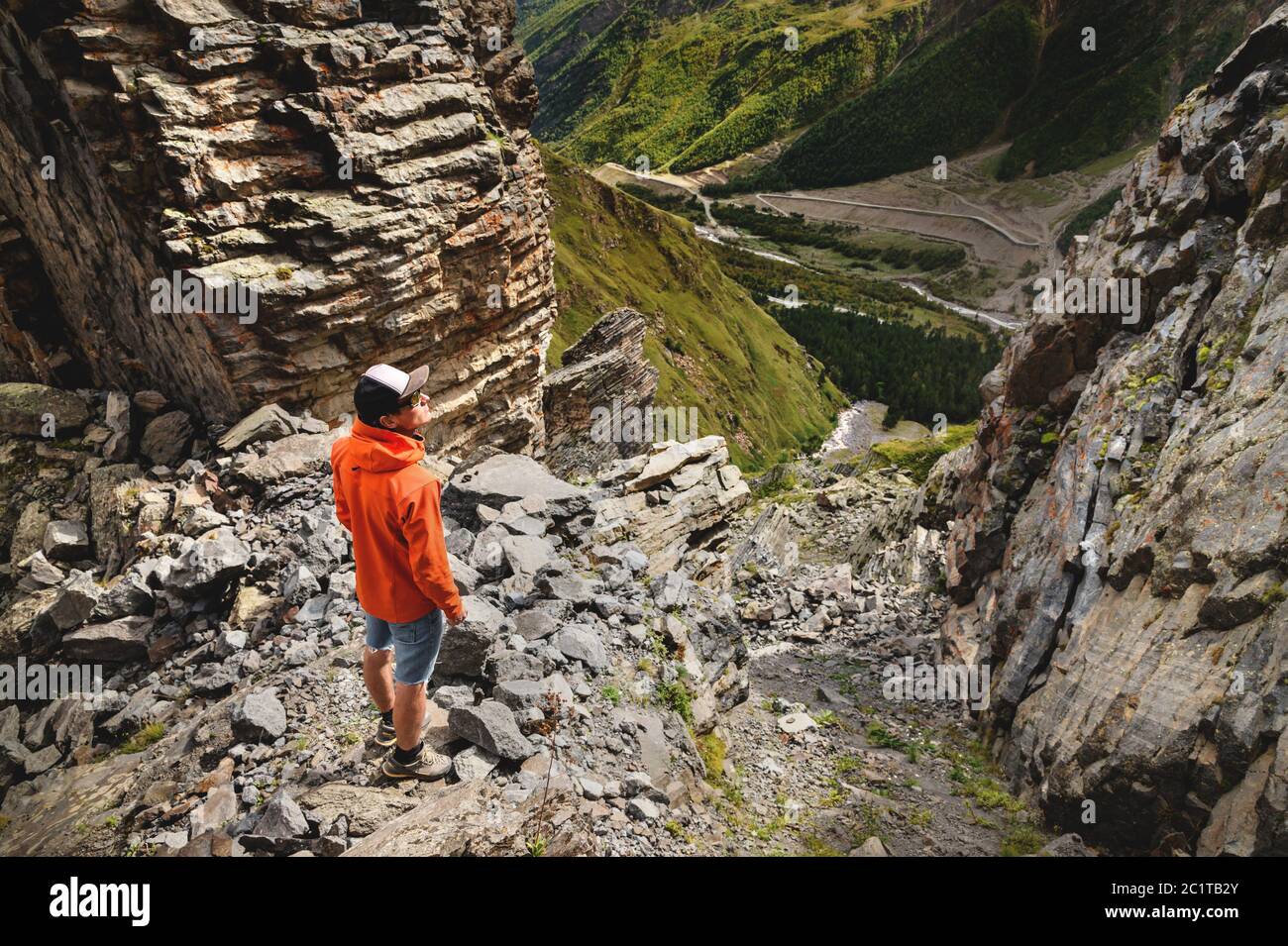 Ritratto di un escursionista maschile in pantaloncini e un cappello dal retro è in piedi su alte rocce al bordo di una scogliera contro lo sfondo Foto Stock