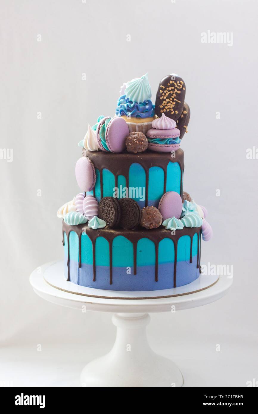 Torta blu a più livelli decorata con cioccolato fondente, cupcake, biscotti, macaroon, meringhe, pop-sicles e barrette di cioccolato. Foto Stock
