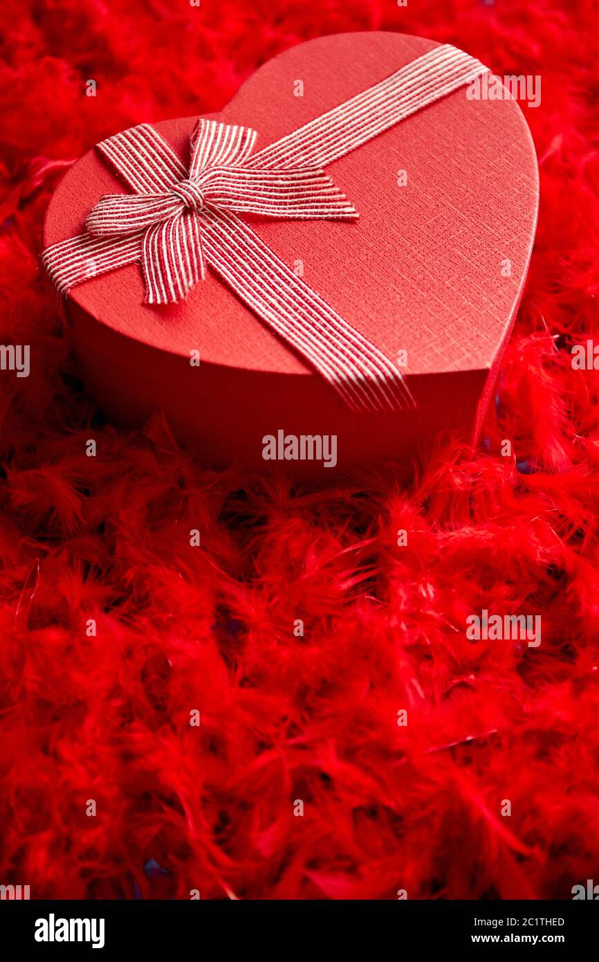 A forma di cuore regalo confezionato, posto sul rosso sfondo piume Foto Stock