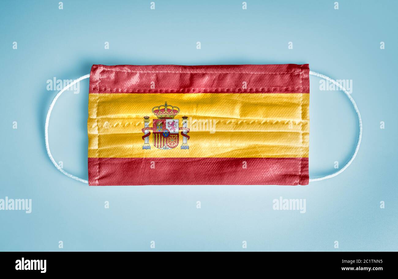 Covid-19 concetto di protezione Coronavirus: Maschera medica monouso con bandiera spagnola su sfondo blu. CHI consiglia l'uso della maschera per la prevenzione Foto Stock