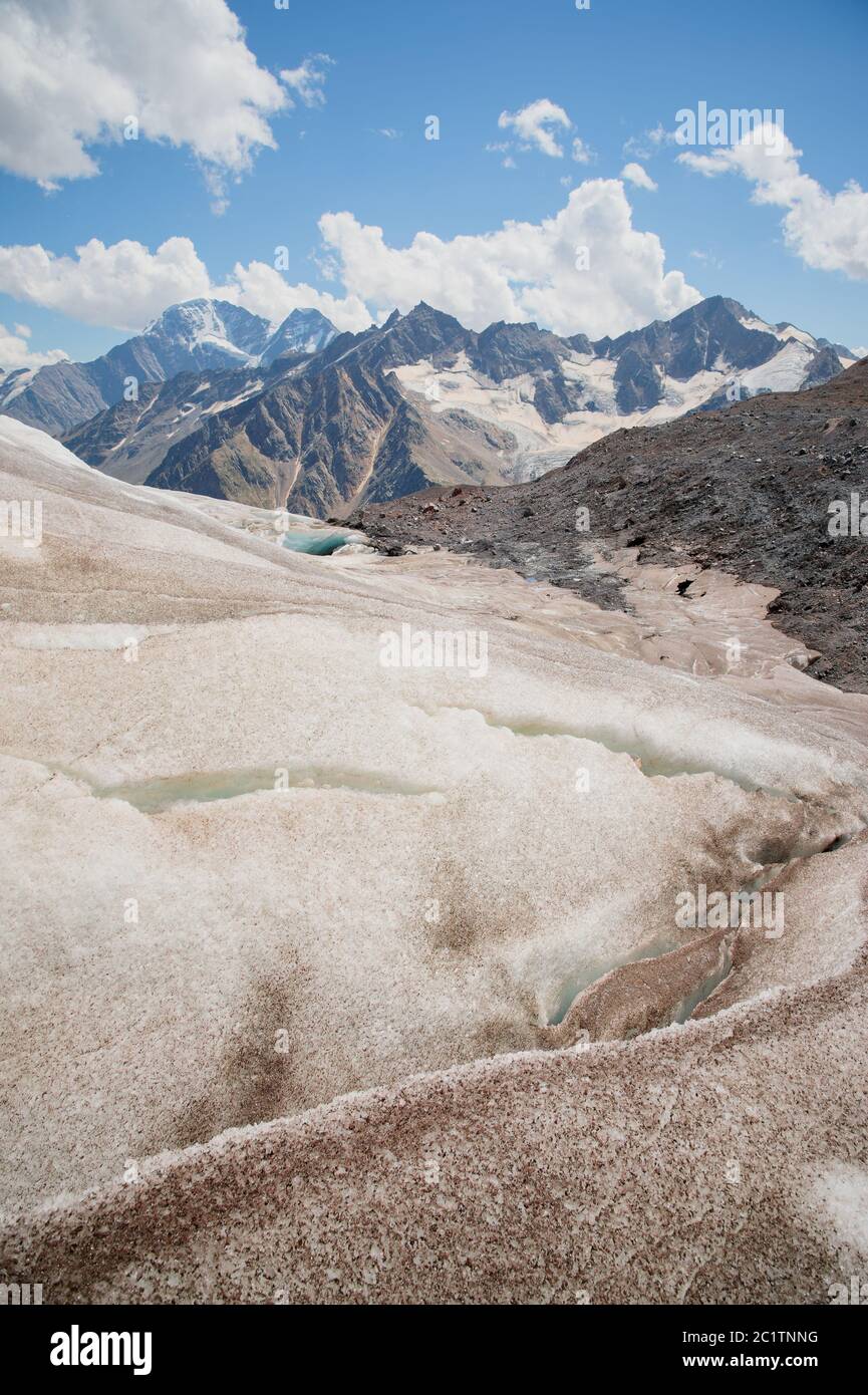 Paesaggio montano polveroso e sporco pendio vulcanico con un ghiacciaio che si scioglie incrinato sullo sfondo delle montagne del Caucaso. Glo Foto Stock