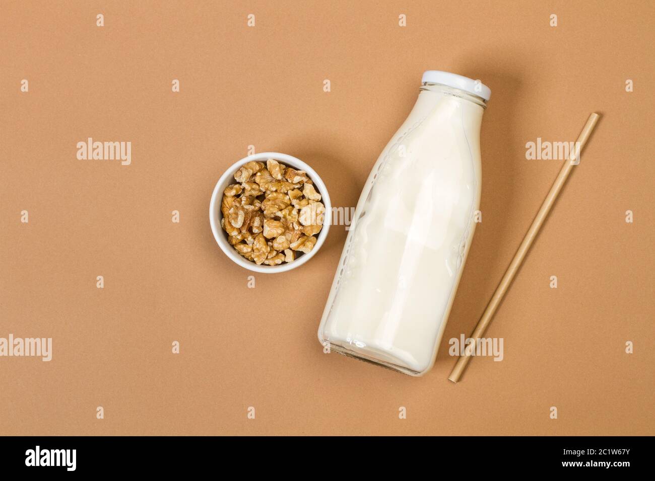 Una bottiglia di latte con noci in un recipiente bianco su sfondo marrone in una vista dall'alto Foto Stock