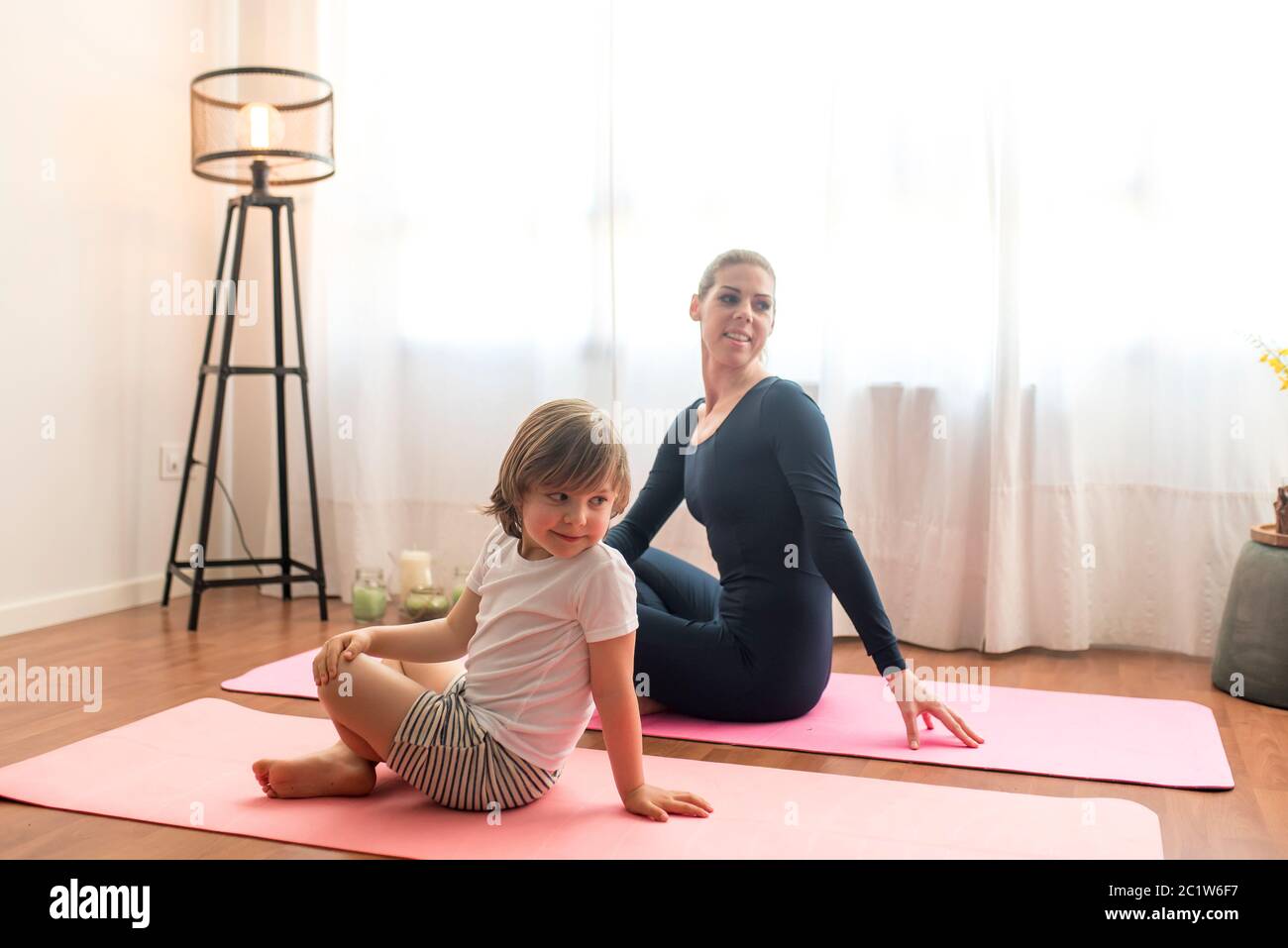 mamma e figlio giovani praticano lo yoga a casa. Madre sportiva con bambino che si esercita al mattino. Mamma e figlio fanno gli esercizi insieme, una famiglia sana l Foto Stock