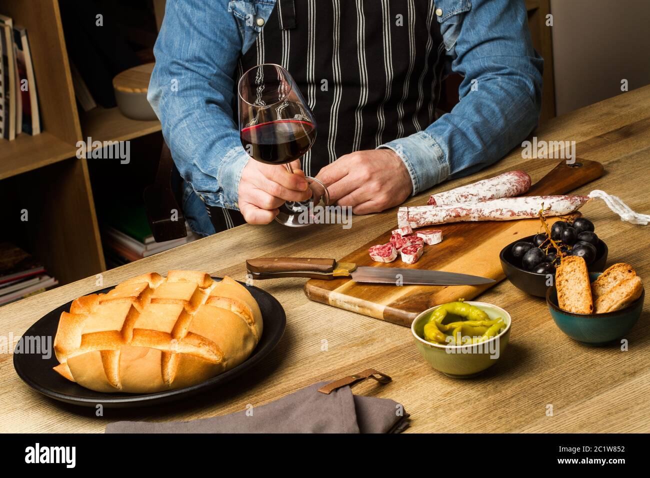Uomo in piedi davanti ad un tavolo con antipasti e un bicchiere di vino in mano Foto Stock