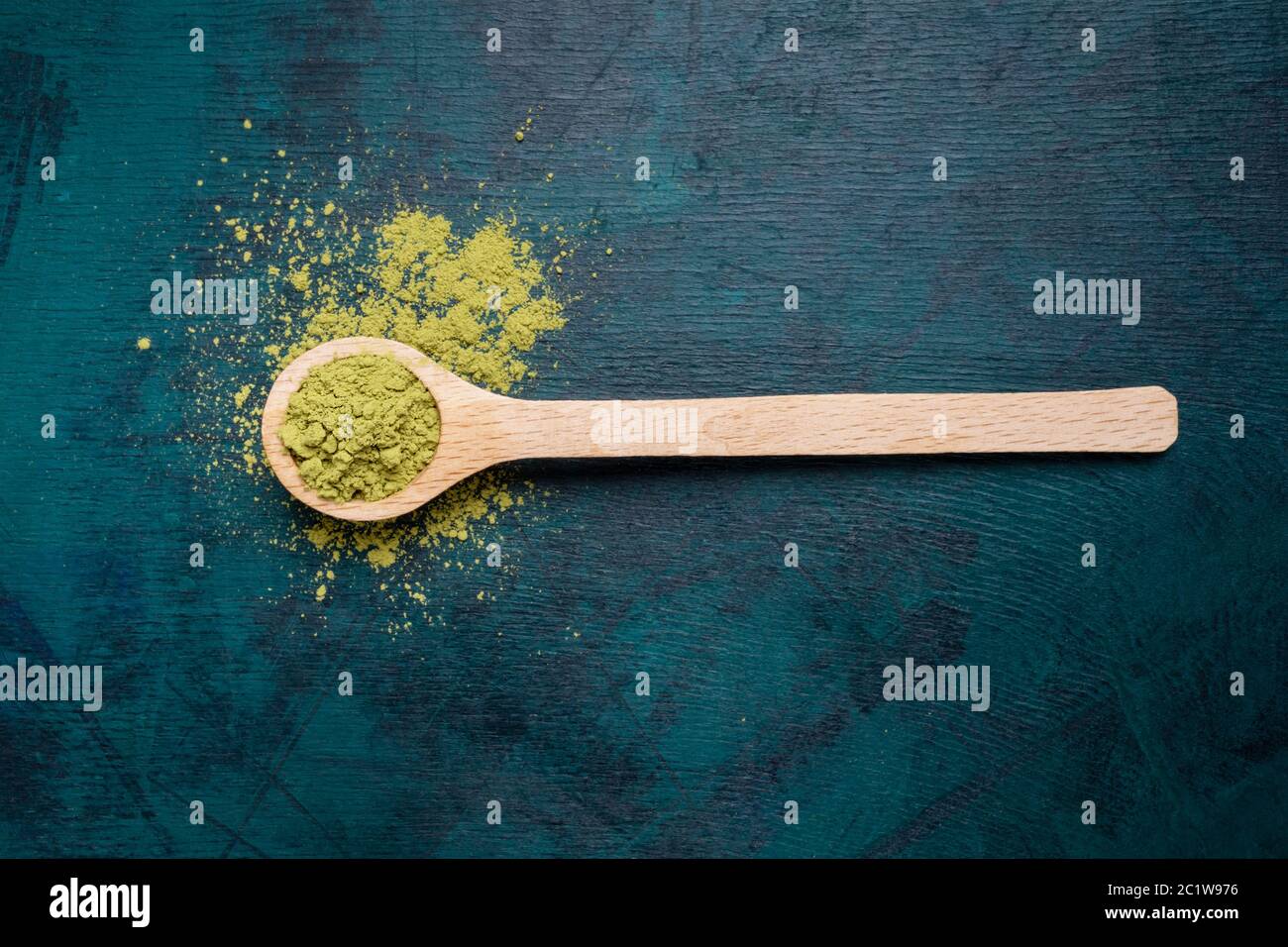 Cucchiaio di legno riempito con polvere di tè verde matcha con un po' di polvere versato su sfondo smeraldo. Il tè giapponese Matcha è un lussuoso bever biologico Foto Stock