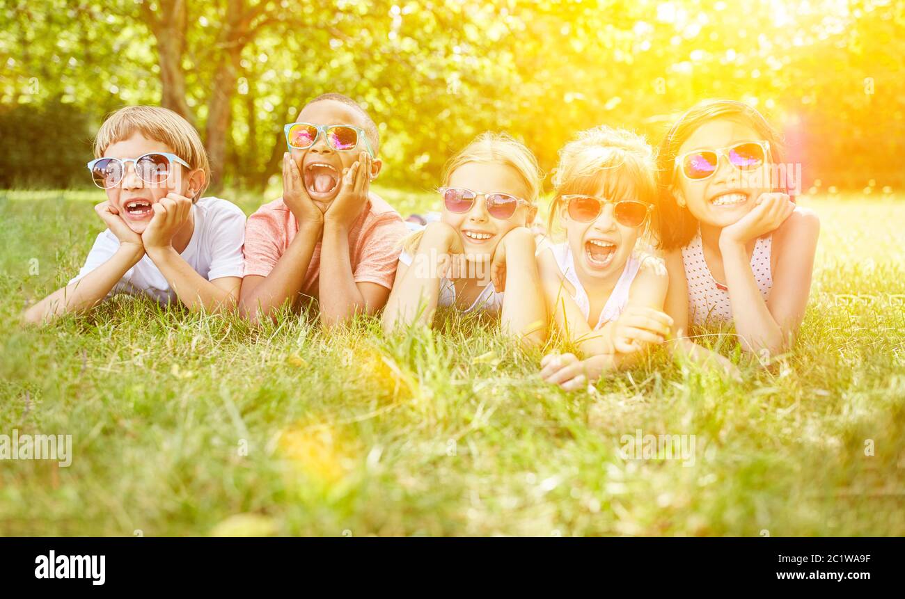 I bambini multiculturali giacciono ridendo con gli occhiali da sole in giardino in estate Foto Stock