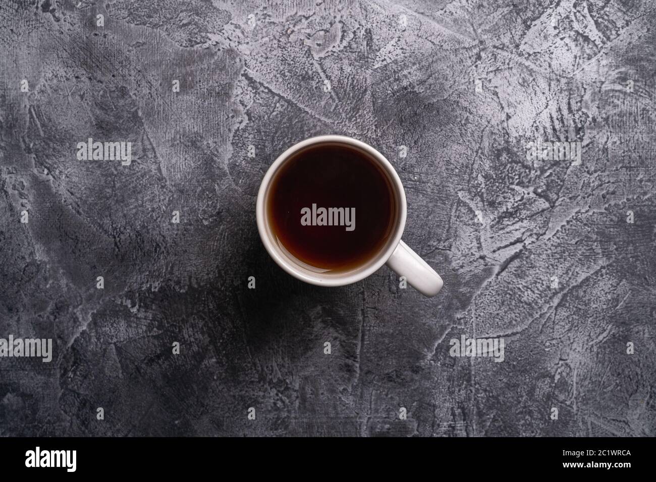 Una tazza in ceramica con tè nero caldo, bevanda in teacup bianco su fondo di pietra scura testurizzata, vista dall'alto Foto Stock