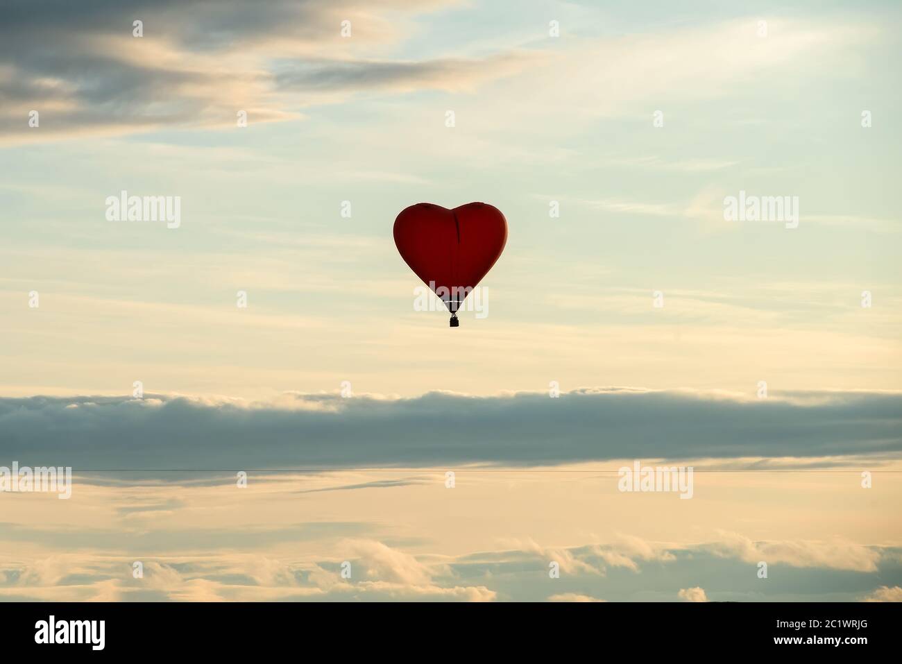 Mongolfiera colorata a forma di cuore che vola contro il cielo nuvoloso Foto Stock