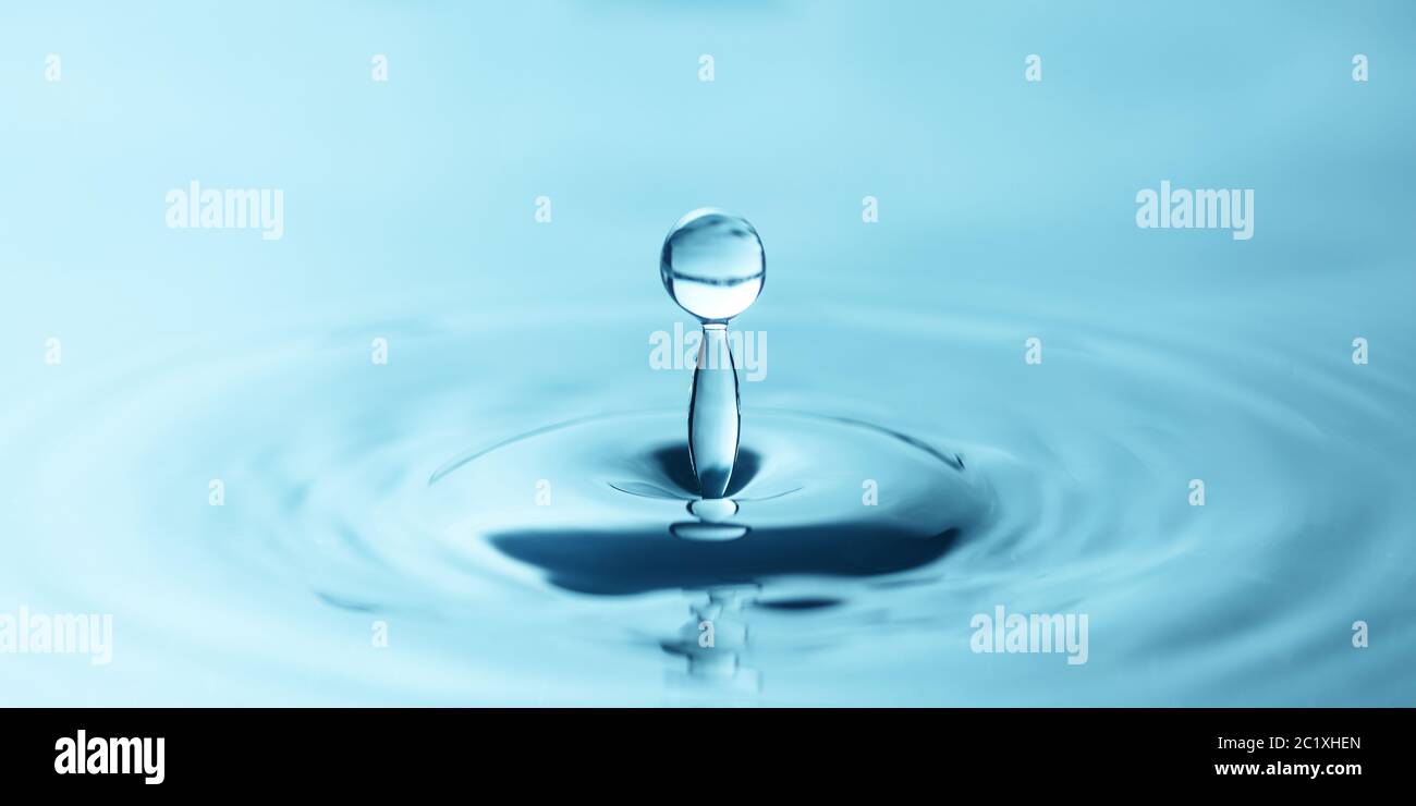 una goccia d'acqua gocciola nell'acqua blu, formando increspature, primo piano Foto Stock