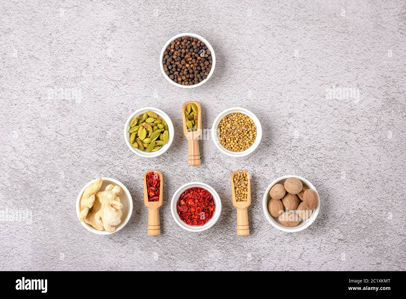 Miscela di spezie aromatiche coriandolo, pepe nero, bergamotto, zenzero secco, noce moscata, paprika in tazze bianche su fondo grigio in calcestruzzo Vista dall'alto posa piatta Foto Stock