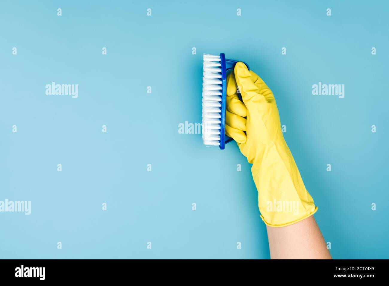 Una mano in un guanto giallo per la casa tiene una spazzola per la pulizia di mobili o del pavimento. Foto Stock