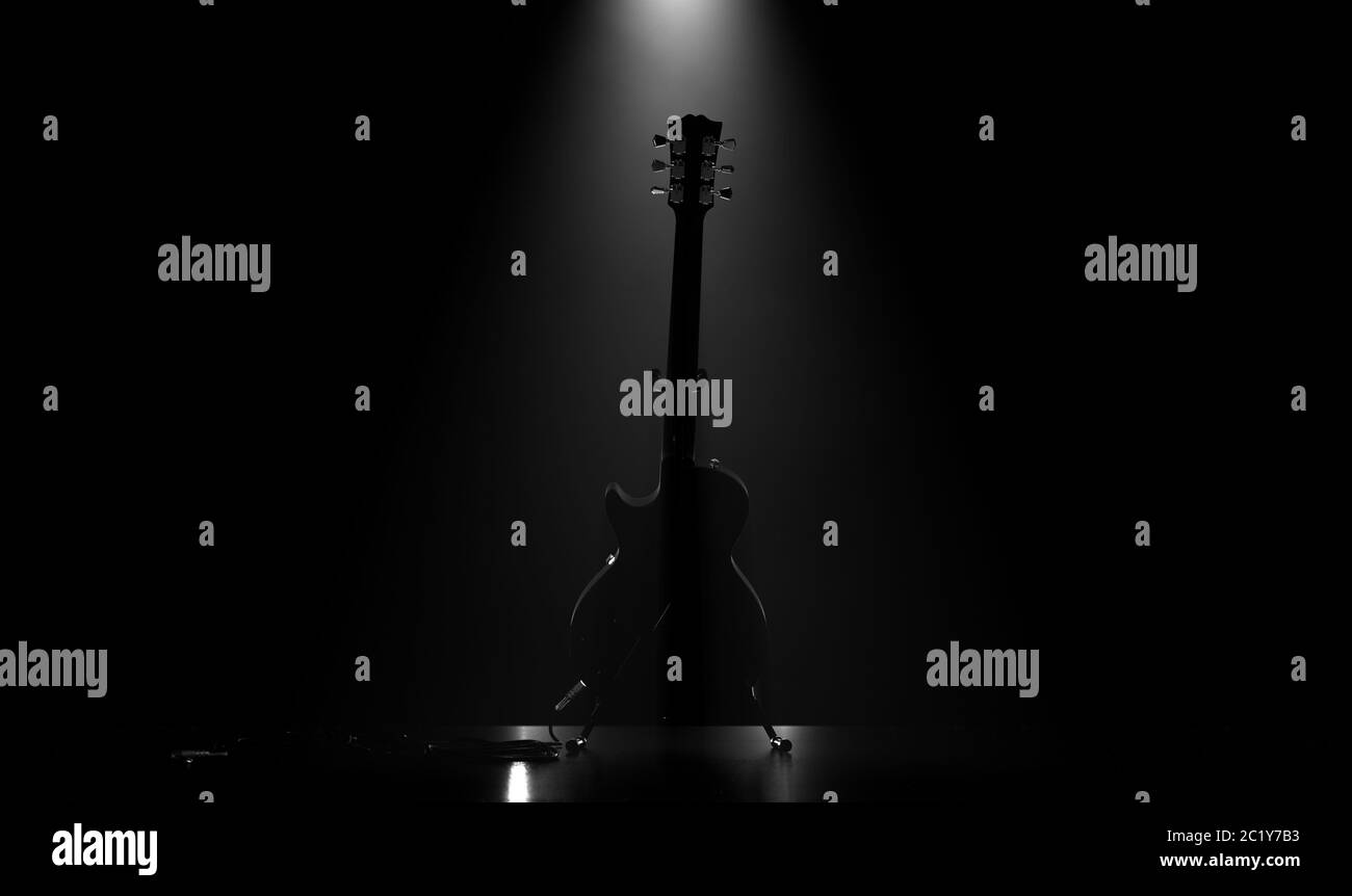 Asilhouette di una chitarra elettrica poggiata su uno stand su un palco di un concerto musicale illuminato da un singolo spot drammatico - rendering 3D Foto Stock
