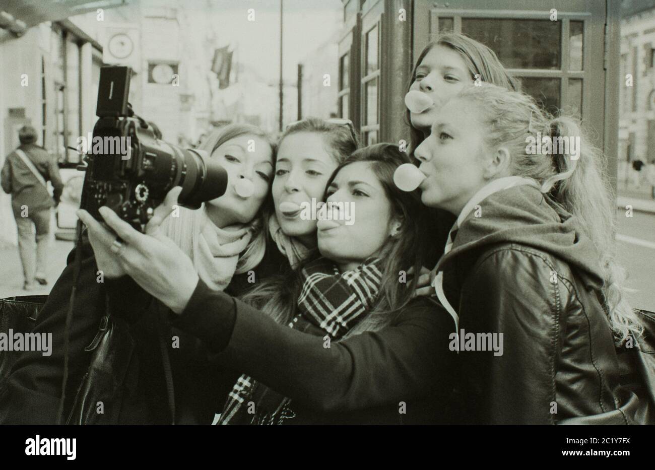 Ragazze masticare gum bubblegher in posa per un selfie utilizzando una fotocamera DSLR, Londra, 2014 Foto Stock