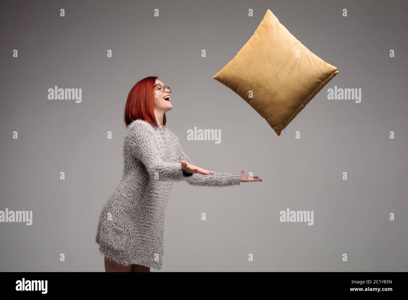 Dai capelli rossi donna in grigio maglione holding e di dare a lato cuscino giallo. Foto Stock