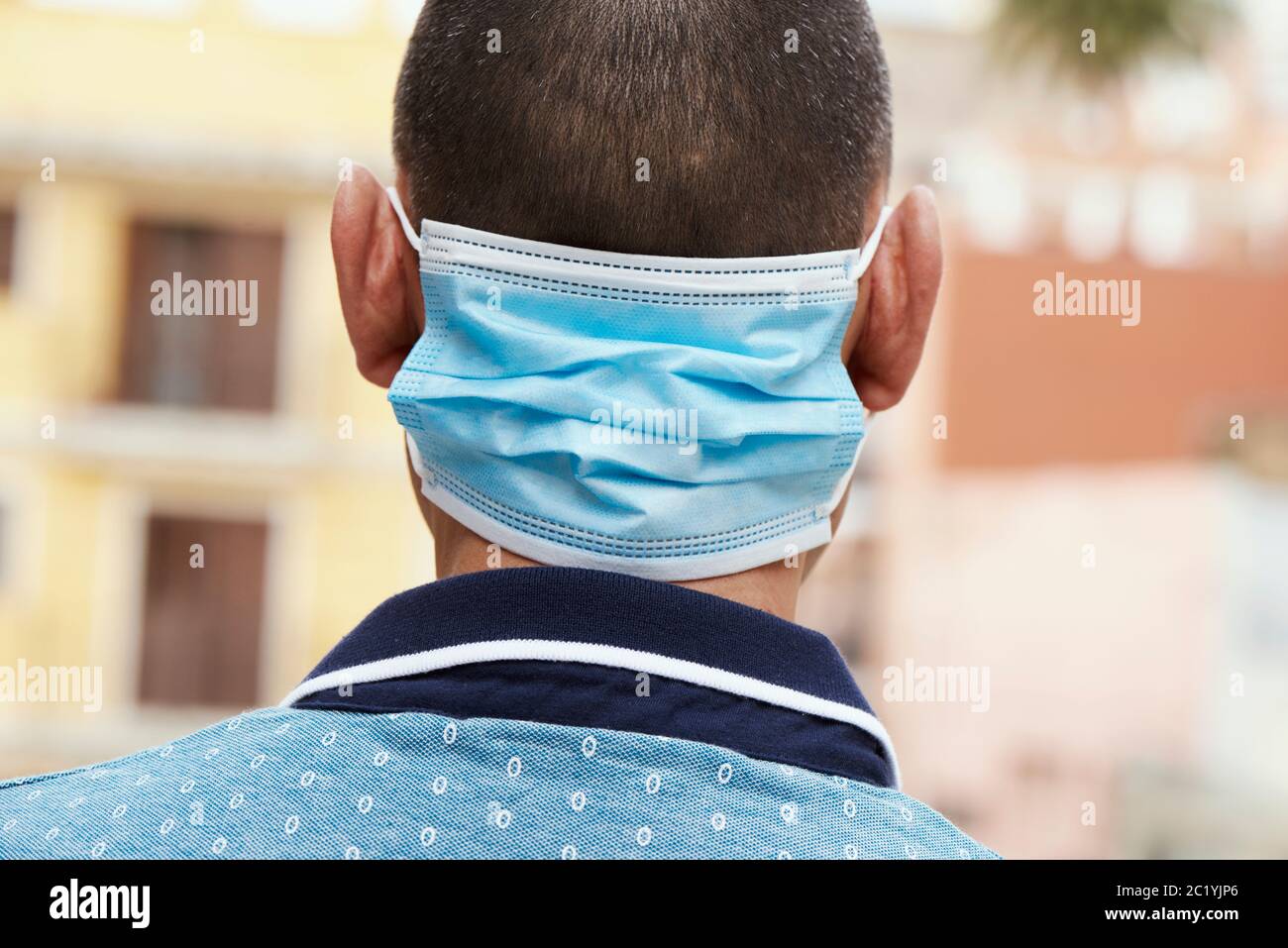 primo piano di un giovane uomo per strada, in abbigliamento casual, indossando la sua maschera chirurgica nella parte posteriore del collo mentre non la indossa in faccia Foto Stock