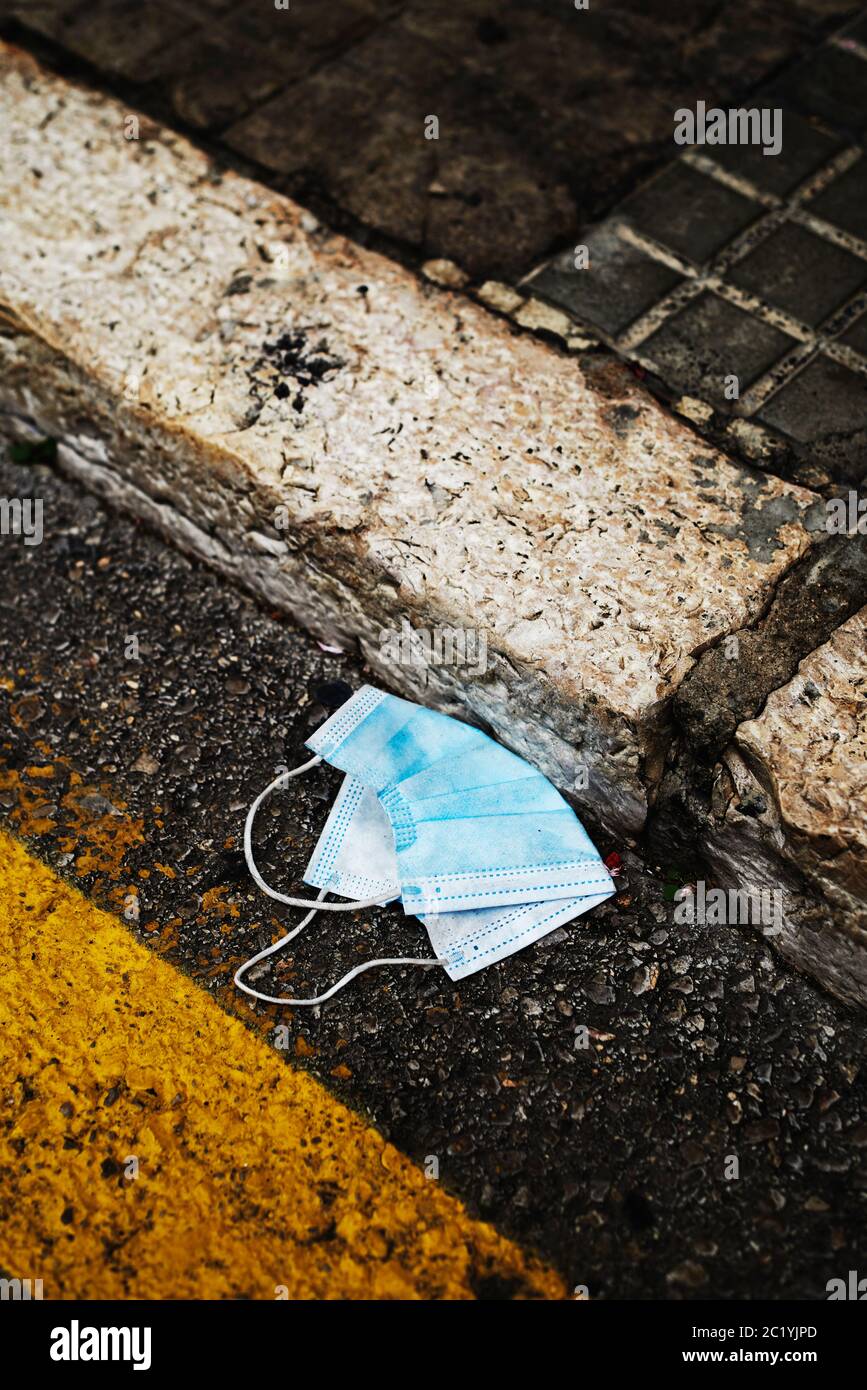 primo piano di una maschera chirurgica blu usata gettata sull'asfalto di una strada cittadina, accanto al marciapiede Foto Stock